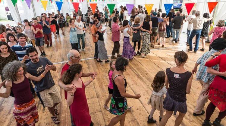 Des festivaliers dansent ensemble toutes générations confondues sous le chapiteau décoré de guirlandes fanions